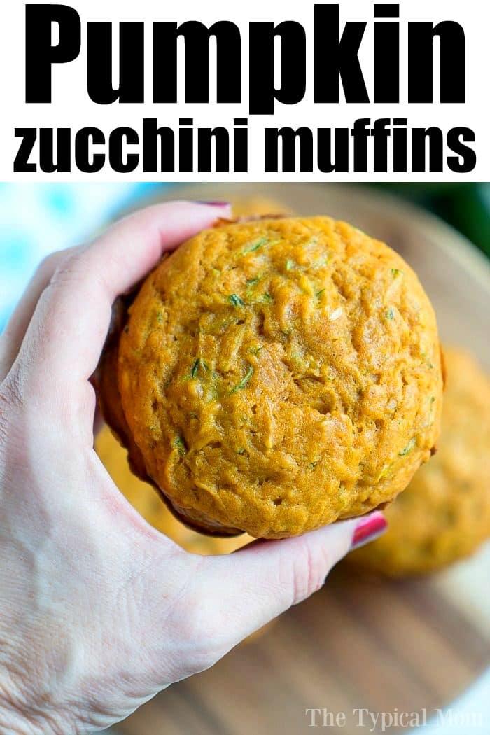 A hand presents a pumpkin zucchini muffin against a wooden board, with the text "Delicious Pumpkin Zucchini Muffins" elegantly displayed above.