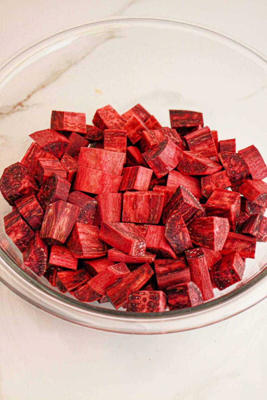 A glass bowl filled with cubed pieces of fresh purple yam, perfect for your next purple sweet potato recipe, rests on a white surface.