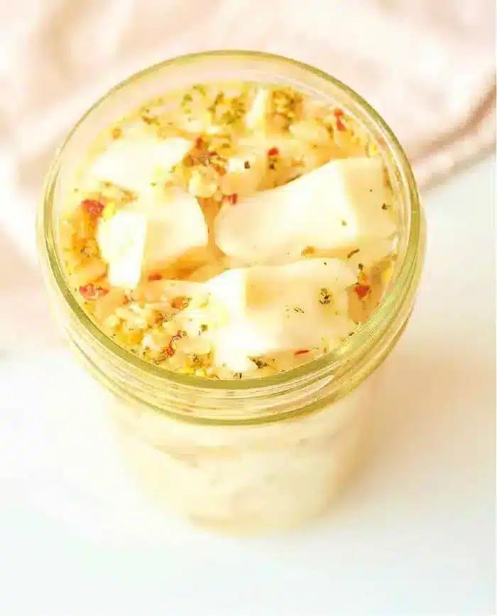 A jar filled with marinated cabbage cubes, topped with herbs and seasoning, sits alongside a vibrant batch of quick-pickled cabbage. The scene is captured from a high angle on a light-colored surface, creating a delightful culinary tableau.