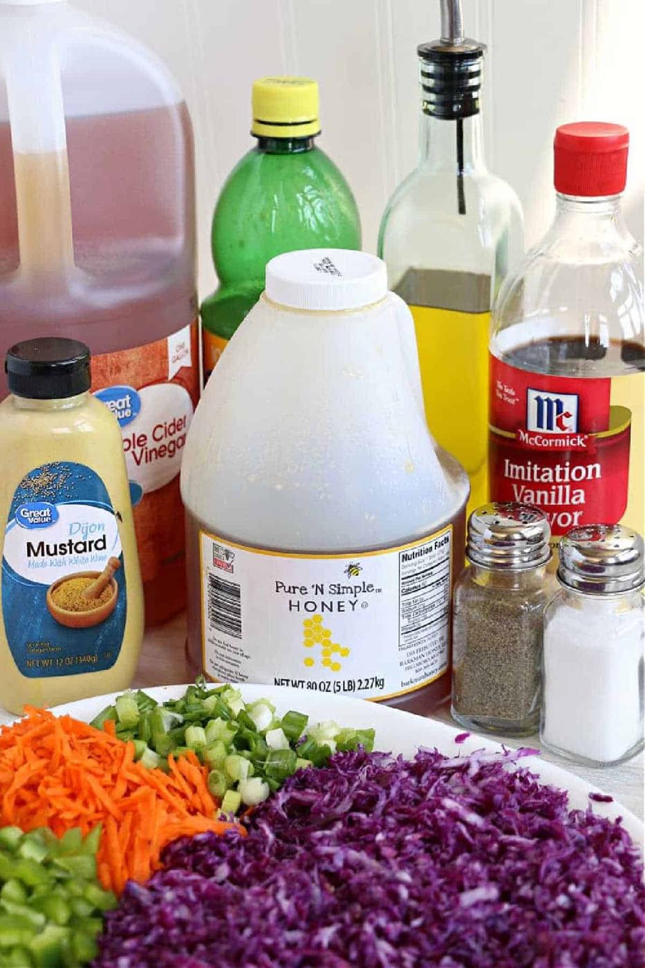 Bottles of condiments and chopped vegetables, including carrots, celery, and red cabbage coleslaw, are arranged on a kitchen counter.