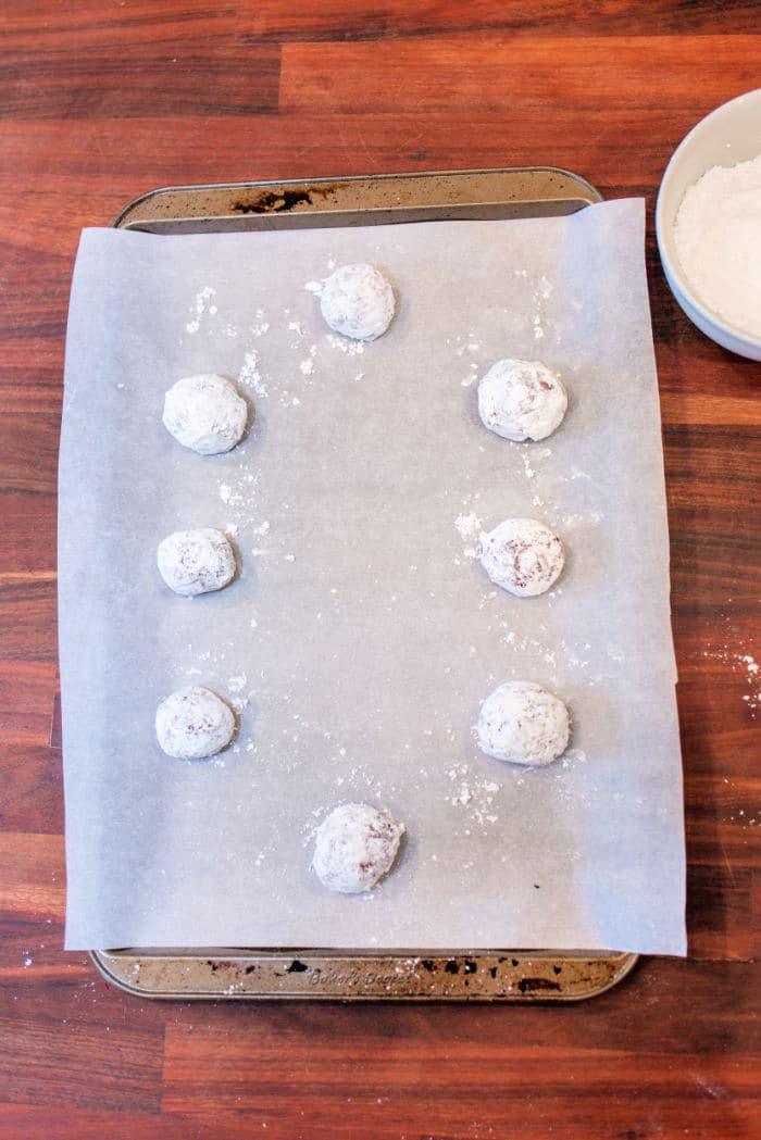 Red Velvet Crinkle Cookies made from cake mix, these raw cookie dough balls are covered in powdered sugar and rest on a parchment-lined baking sheet.