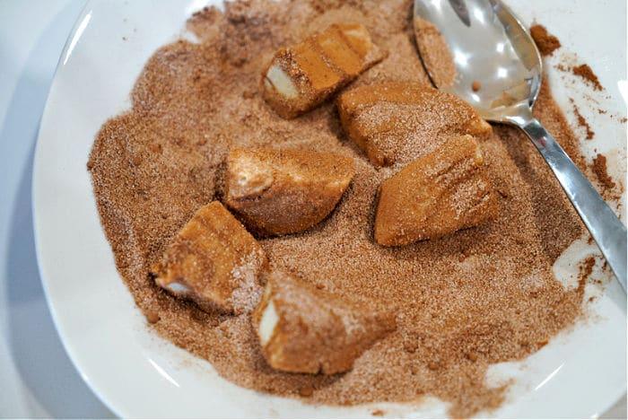 cinnamon roll slices coated in cinnamon sugar on a white plate with a spoon, reminiscent of the comforting allure of Rhodes monkey bread.