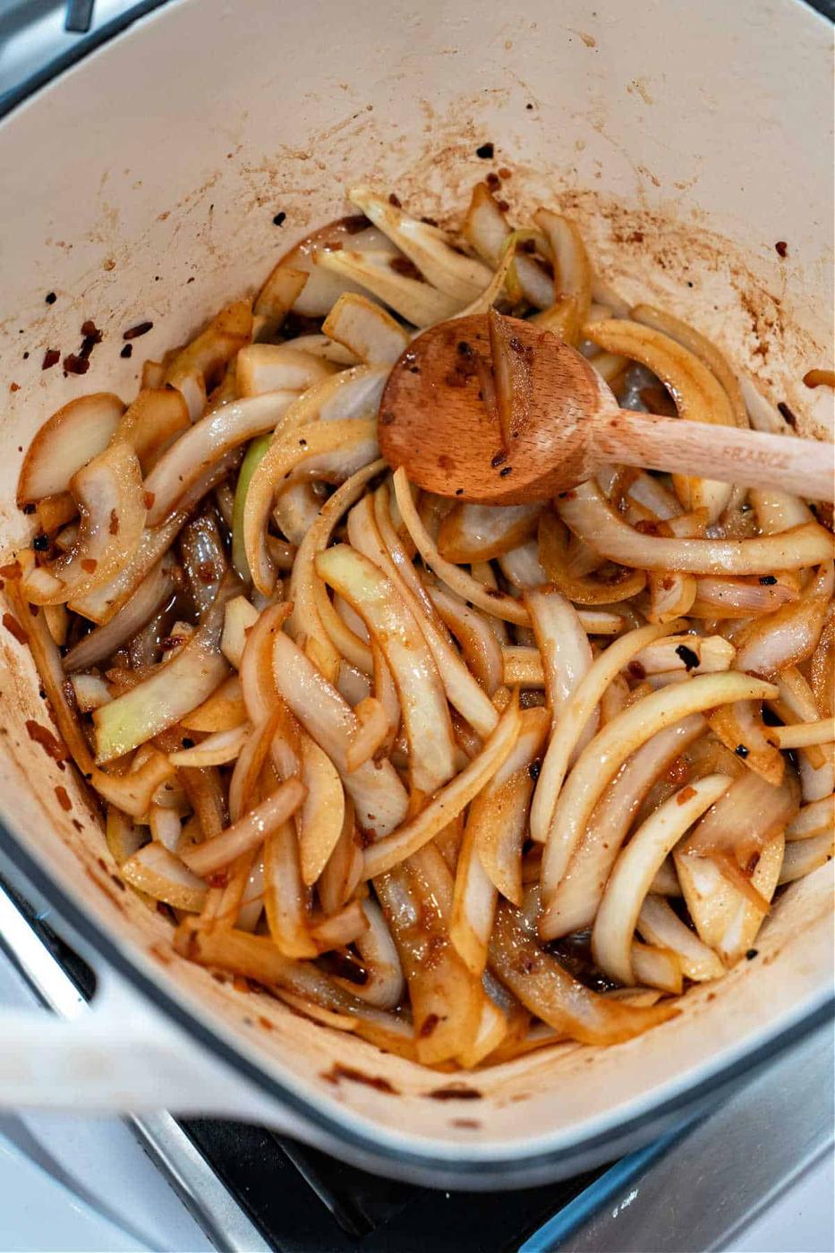 Sliced onions roasting in a pot, seasoned to perfection and stirred with a wooden spoon.