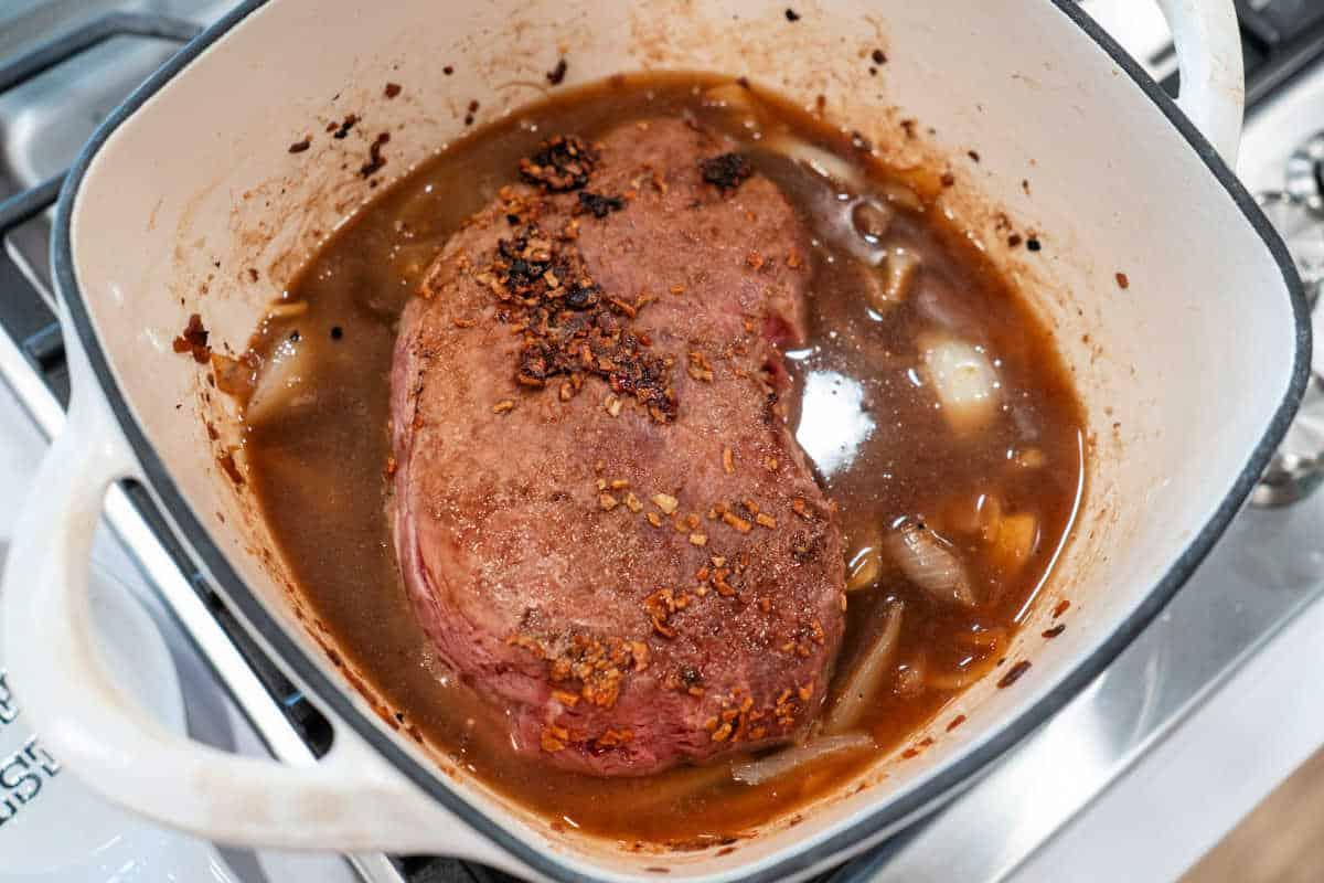 Savory roast beef simmered gently in a pot with caramelized onions and hearty broth on the stove.