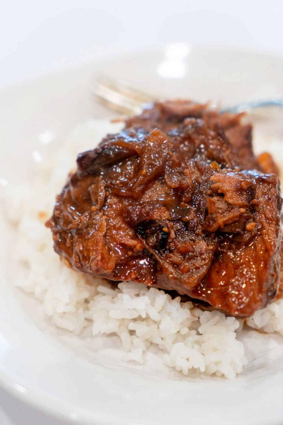A plate of fragrant white rice topped with braised meat and roasted onions in a rich, dark sauce.