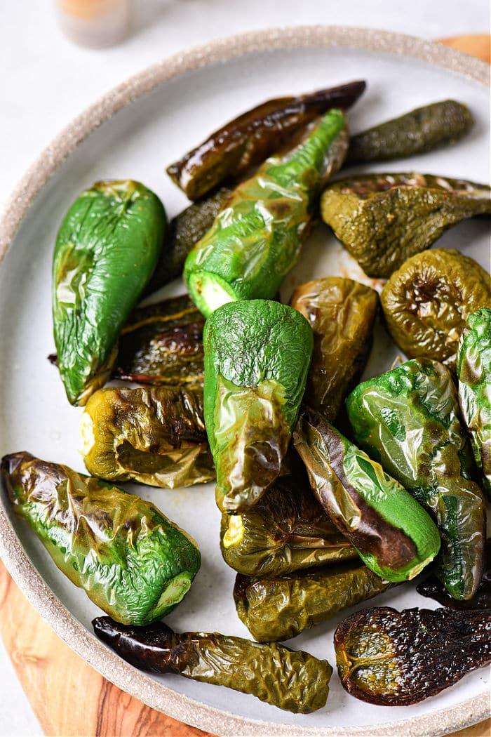 Roasted jalapeno peppers in oven, vibrant and smoky, rest elegantly on a ceramic plate.
