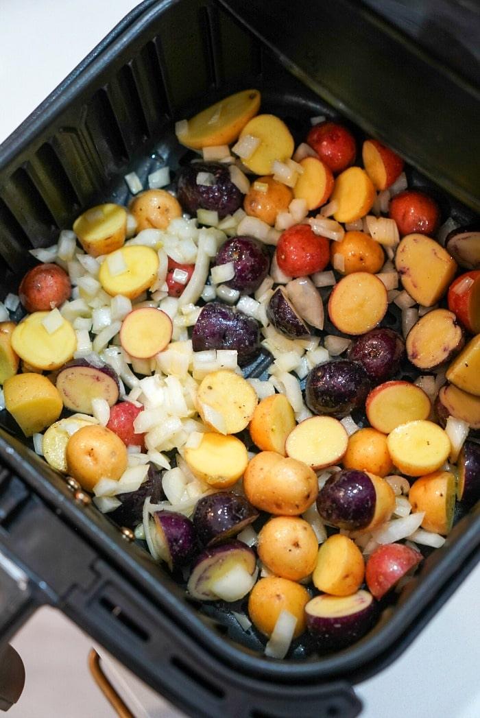 Roasted potatoes in an air fryer, mixed with vibrant chopped onions, are perfectly arranged in the basket and ready for cooking.
