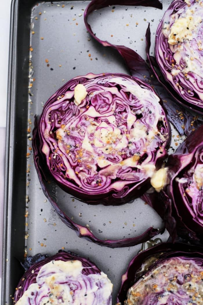 Sliced purple cabbage, also known as roasted red cabbage, is roasted on a baking sheet with melted butter and seasonings.