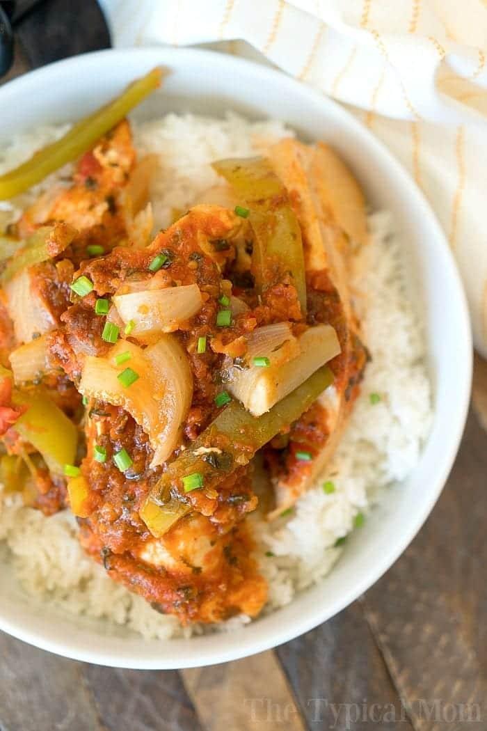 A bowl of white rice topped with slow cooker salsa chicken, bell peppers, onions, and chopped green herbs.