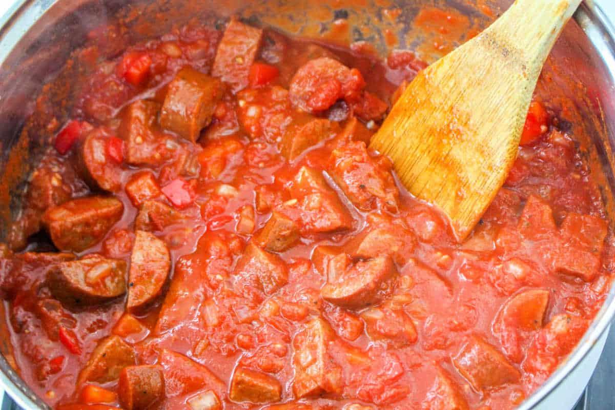 A pot of chunky tomato sauce with sausages sits invitingly, its rich aroma filling the air. Next to it, a wooden spoon rests, ready to twirl into a perfect blend reminiscent of sausage spaghetti.