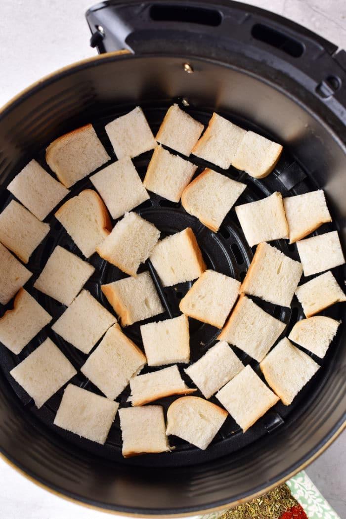 Cubed bread pieces spread evenly in an air fryer basket, perfect for making seasoned breadcrumbs or toasting until golden brown.