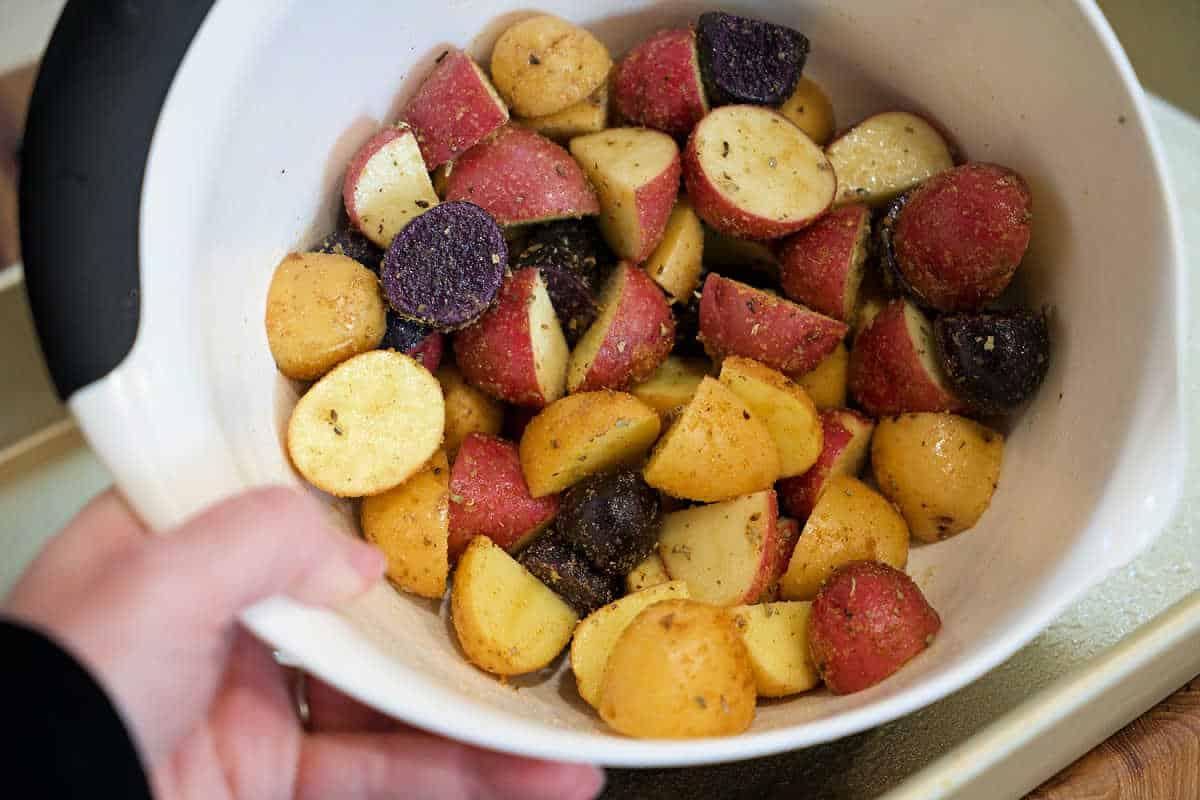 A bowl of seasoned, chopped red, yellow, and purple potatoes is ready for roasting—perfect to pair with shrimp and potatoes for a hearty meal.