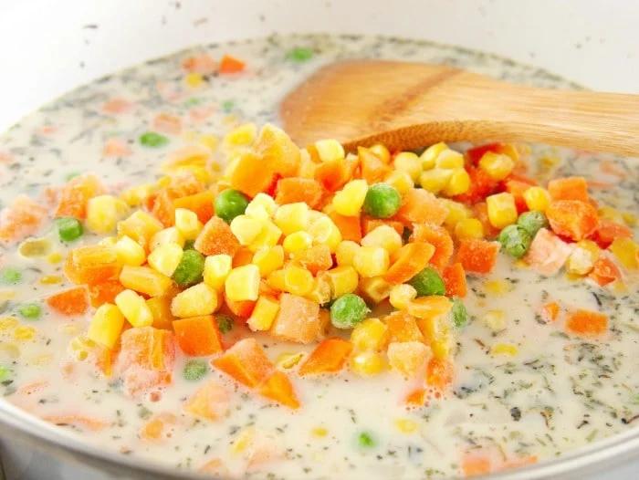 Simple chicken pot pie filling recipe, being stirred with a wooden spoon.