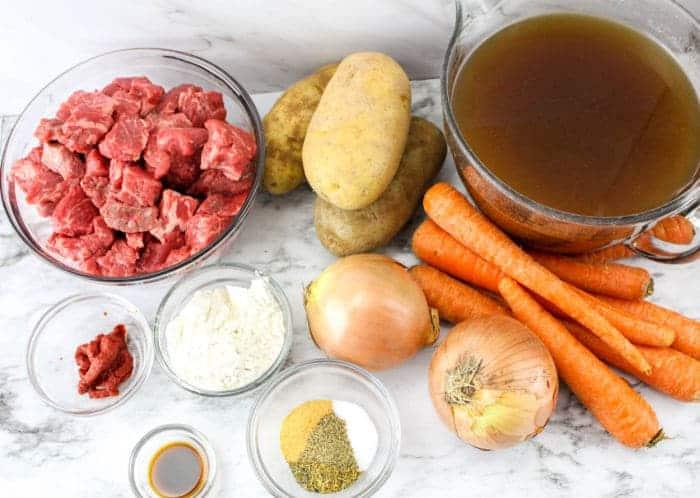 Raw beef, potatoes, carrots, onions, broth, flour, tomato paste, spices, and sauce on a marble surface—perfect for making Slow Cooker Beef Stew with Onion Soup Mix.