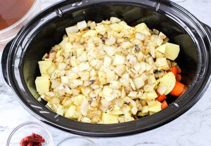 Diced potatoes, onions, and carrots in a black slow cooker, perfect for making Slow Cooker Beef Stew with Onion Soup Mix.