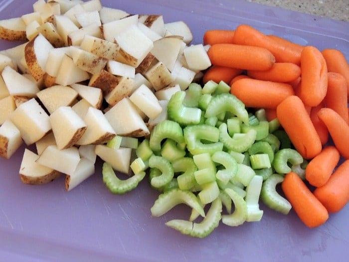 Chopped potatoes, celery slices, and baby carrots on a purple cutting board, perfect for preparing slow cooker chicken and dumplings.