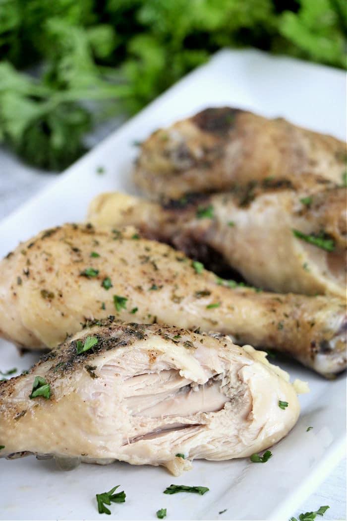 Slow-cooked chicken legs rest on a white plate, garnished with fresh herbs.