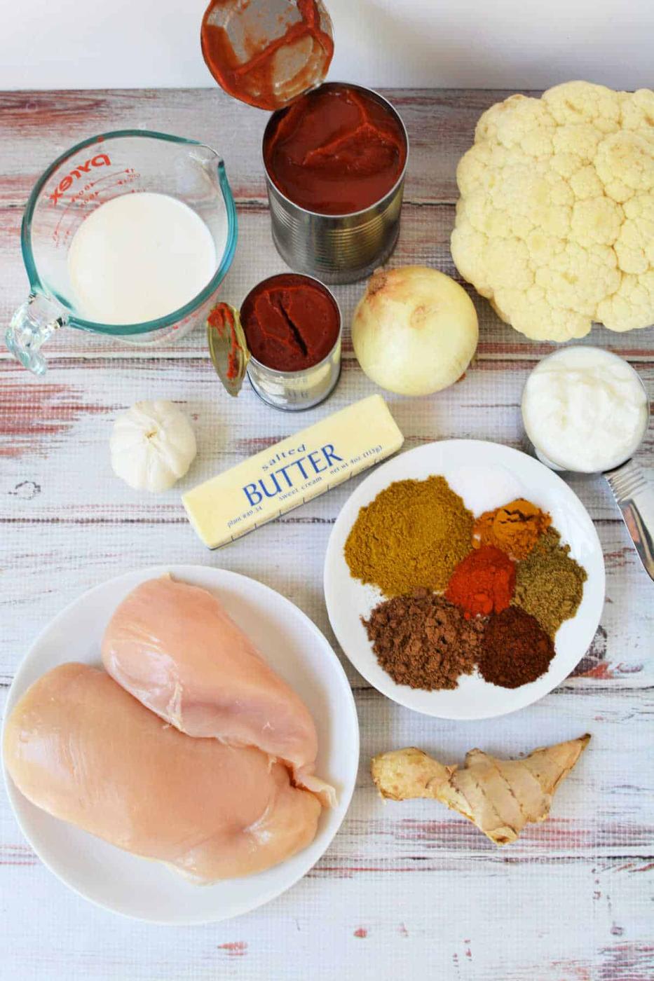 Ingredients for a delicious Slow Cooker Chicken Makhani dish, including chicken, spices, onion, garlic, butter, cauliflower, and tomato paste.