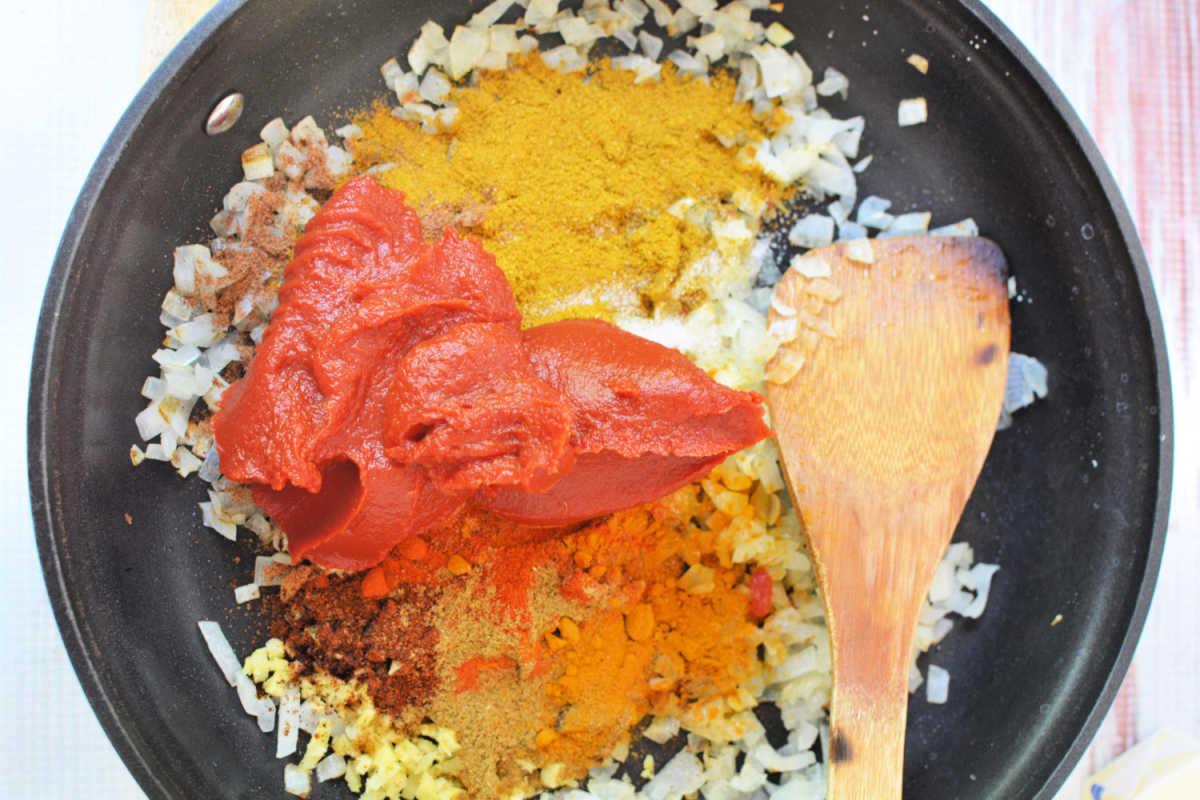 Chopped onions, spices, and tomato paste in a skillet with a wooden spatula—perfect for starting a rich Chicken Makhani before transferring to the slow cooker.