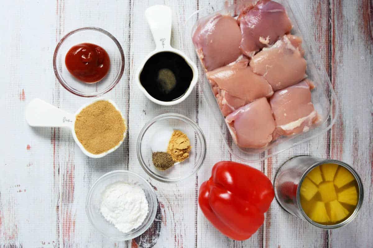Raw chicken thighs, red bell pepper, canned pineapple, and small bowls of ketchup, spices, soy sauce, cornstarch, and a splash of pineapple juice—perfect for an easy Slow Cooker Chicken recipe.