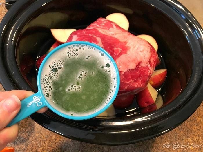 A person pours beer over a corned beef brisket in a slow cooker with potatoes, perfecting this succulent dish.