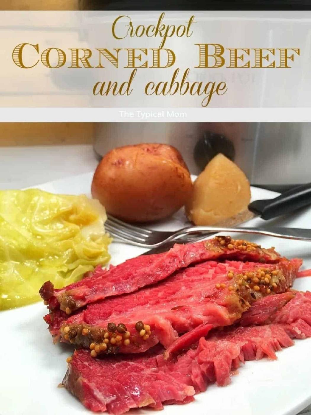 Sliced slow cooker corned beef brisket with mustard seeds, cabbage, and potatoes on a plate in front of a crockpot.