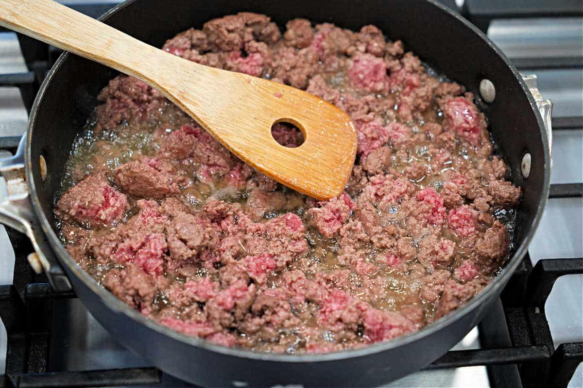 Ground beef being browned in a skillet on a stove, stirred with a wooden spatula—perfect for starting a hearty slow cooker stroganoff.