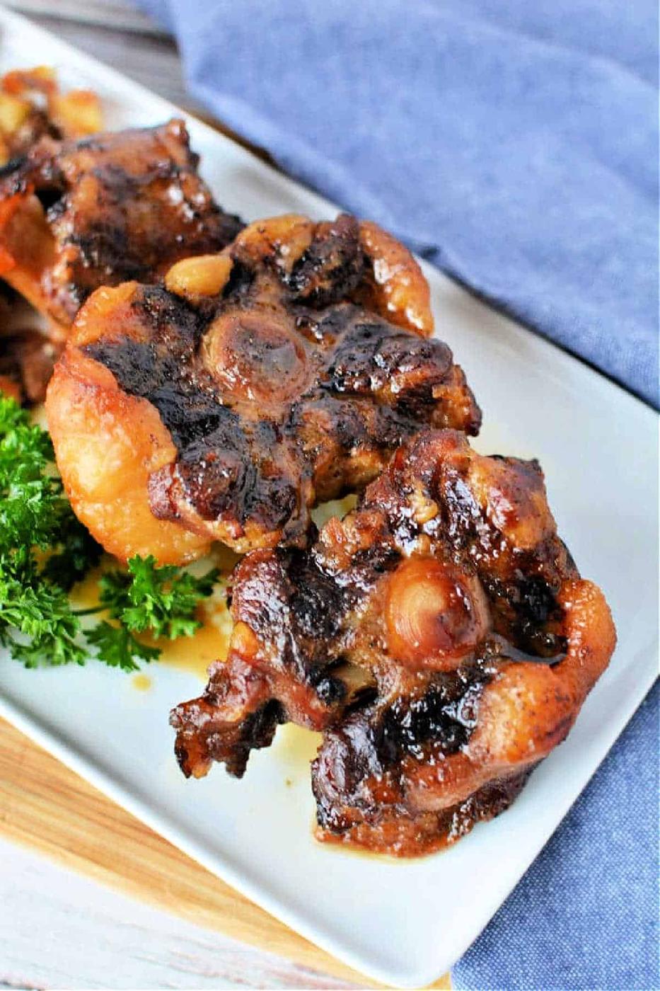 Close-up of oxtail pieces on a white plate, garnished with fresh parsley. This dish captures the rich flavors reminiscent of slow cooker oxtail perfection.