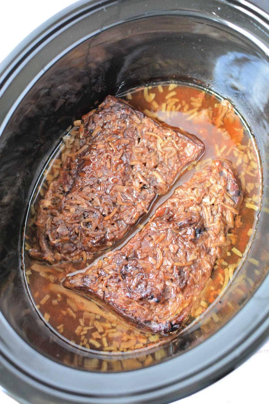 Two pieces of beef brisket cook in a slow cooker with broth and seasonings, just like you would prepare Slow Cooker Skirt Steak for tender, flavorful results.