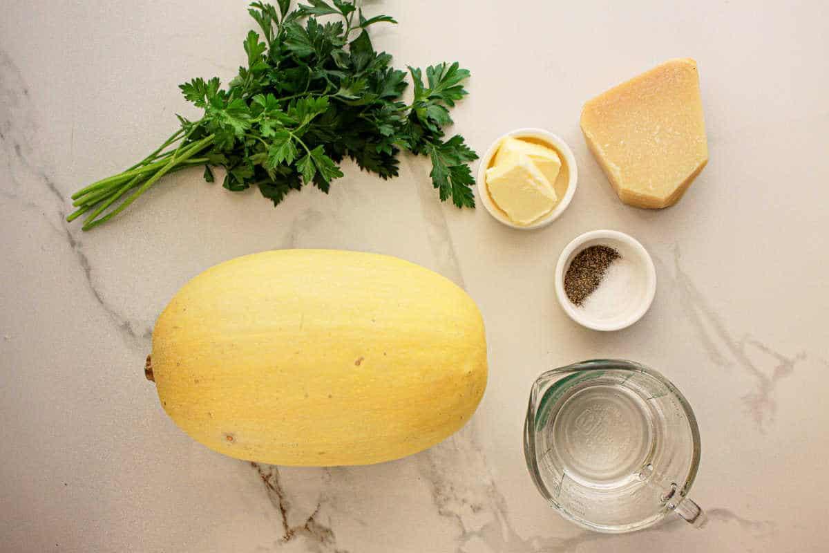Slow Cooker Spaghetti Squash, parsley, butter, Parmesan, salt, pepper, and water rest on a marble countertop.