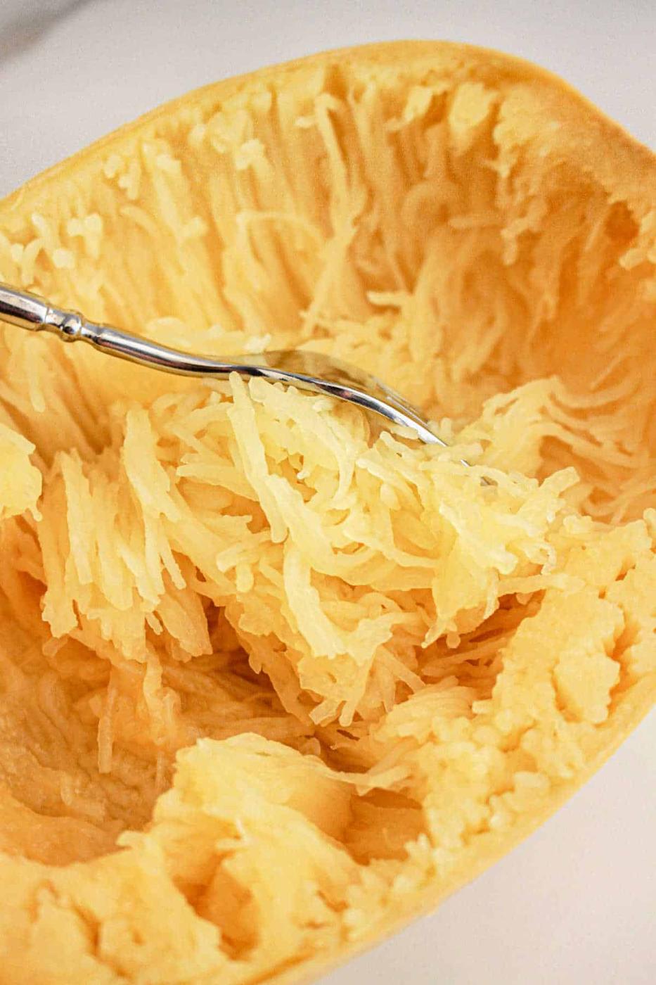 Using a fork, gently scrape spaghetti squash strands inside a halved squash shell, effortlessly prepared in the slow cooker for a tender and flavorful meal.