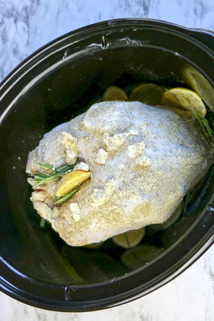 This slow cooker turkey crown recipe features raw turkey breast seasoned with herbs and lemon slices for a succulent meal.