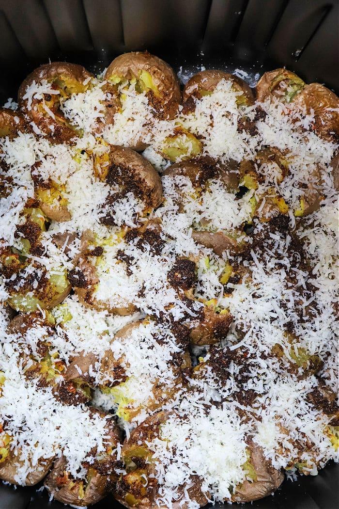 Smashed potatoes in ninja foodi topped with melted cheese and breadcrumbs, all perfectly crisped up in a black pan.