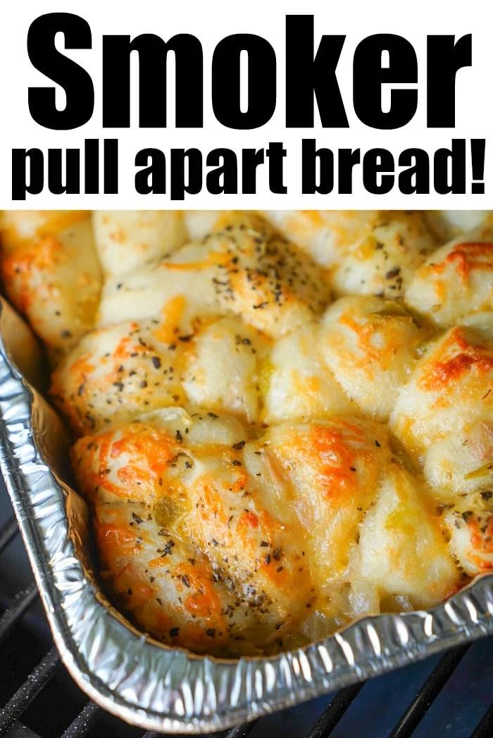 A rectangular foil tray filled with pull-apart smoked bread, topped with herbs and melted cheese. The bread appears to be cooked on a smoker. Text on the image reads: Smoker pull apart bread!