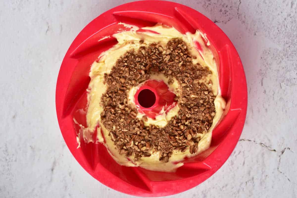 Bundt pan with cake batter, using the classic Sock it to me cake recipe with cake mix, topped with a crumble layer and placed on a textured light surface.