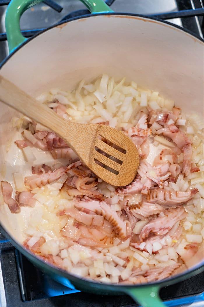 Chopped onions and bacon cooking in a pot with a wooden spoon on a stove—perfect beginnings for classic Southern Fried Cabbage.