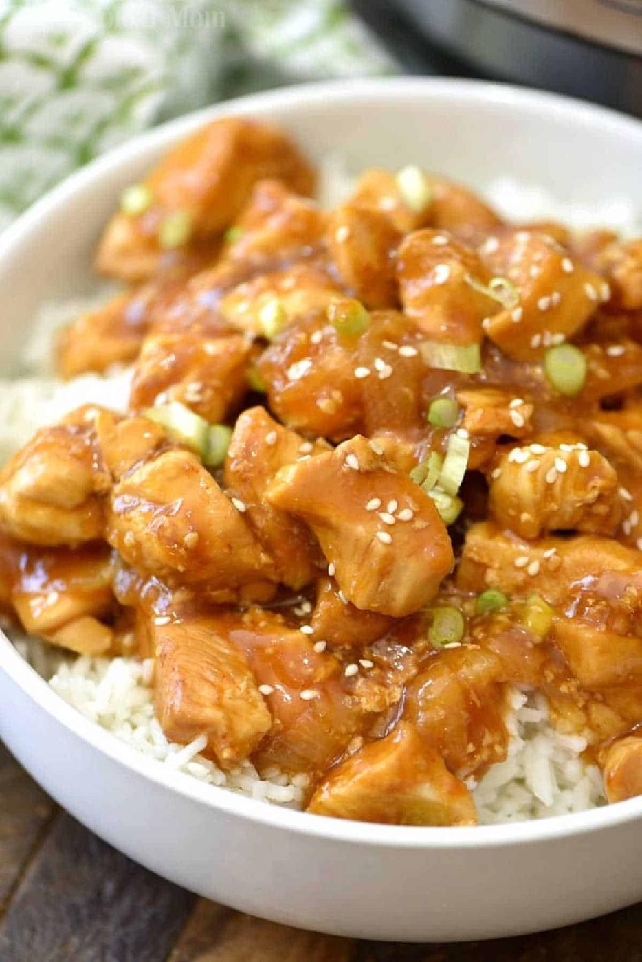 A bowl of white rice topped with spicy honey Instant Pot chicken, sliced green onions, and sesame seeds.
