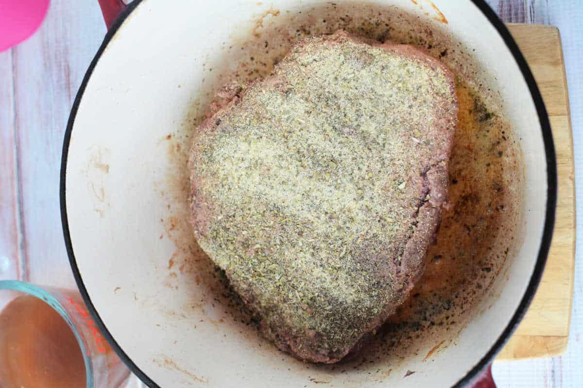 A seasoned raw meat roast sits in a pot, poised for cooking into a delicious stove top pot roast.