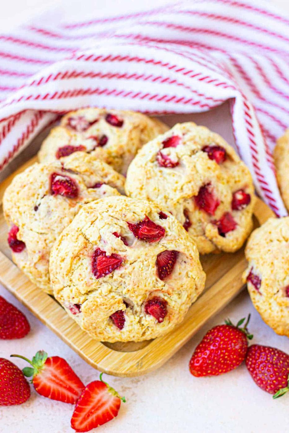 biscuits with strawberries on a wooden tray, surrounded by fresh strawberries and a striped cloth, resemble delightful strawberry biscuits ready for a morning treat.