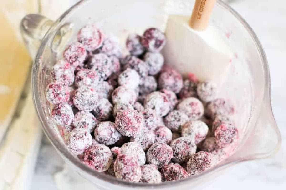 Glass bowl of fresh cranberries coated in sugar, with a white spatula inside the bowl—perfect for adding a sweet-tart twist to your next strudel pastry.