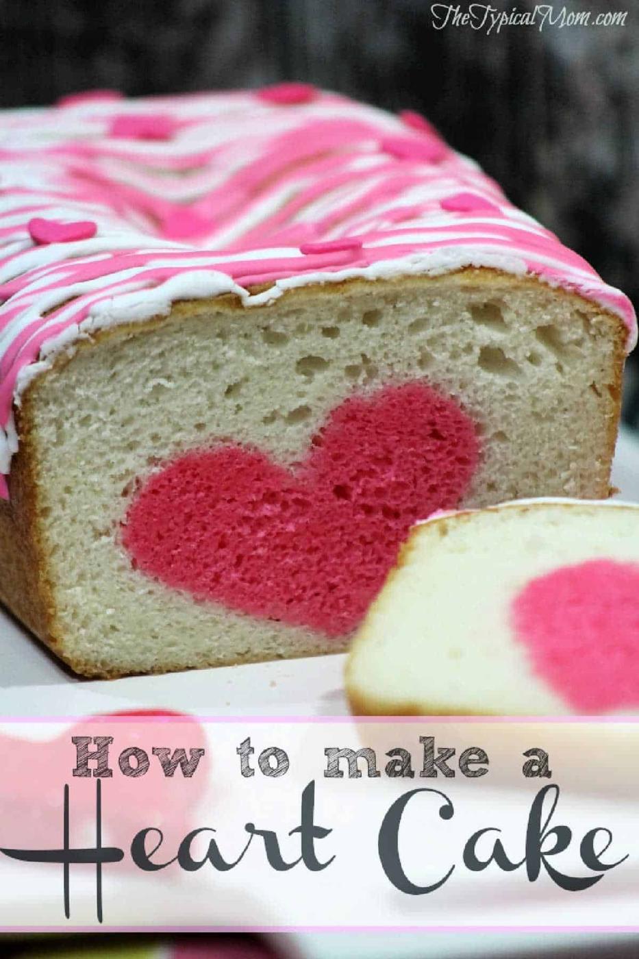 A surprise inside cake loaf with a pink heart shape in the center, topped with pink and white icing, and a sliced piece in front.