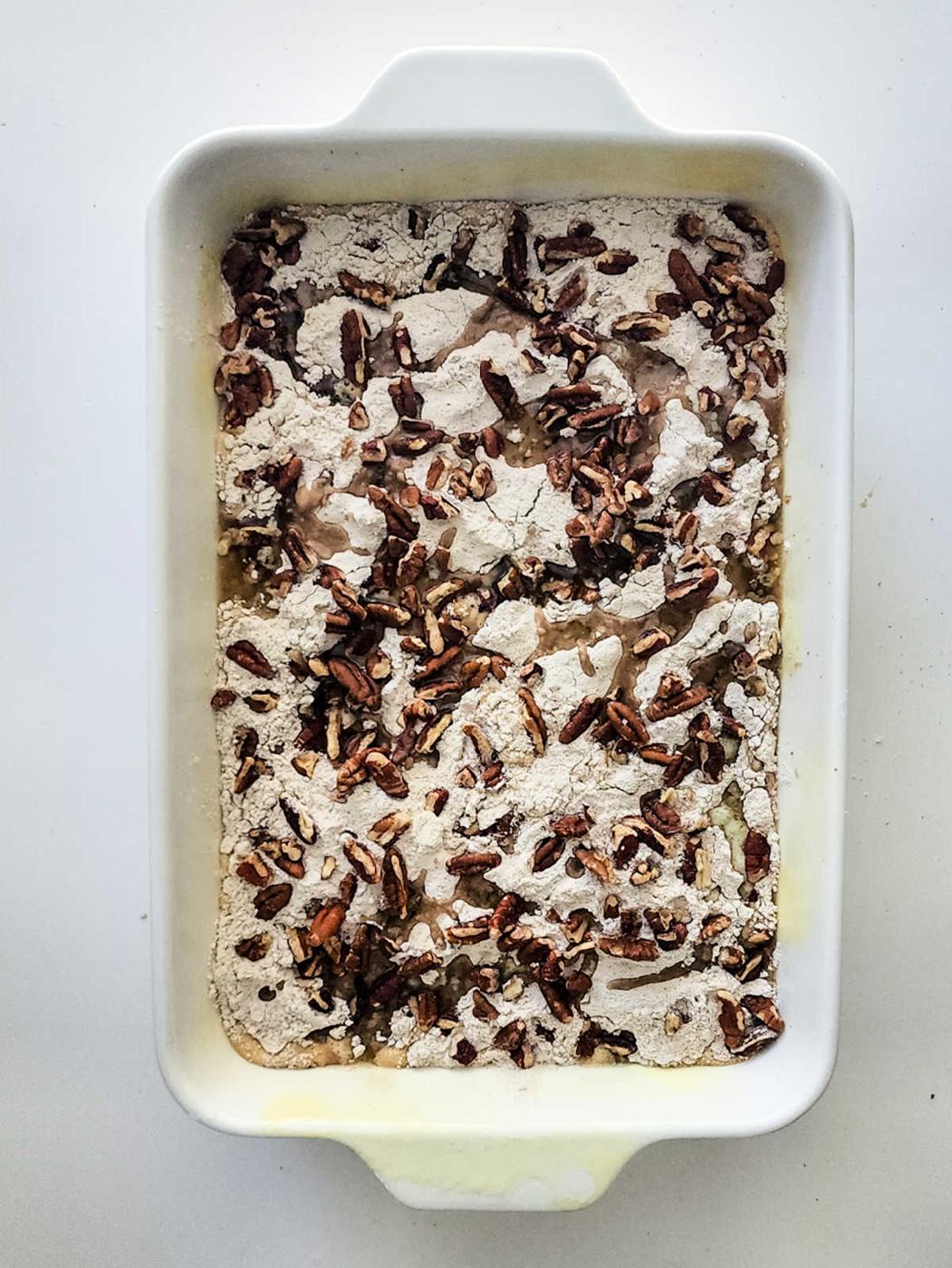 Rectangular baking dish with flour mixture and chopped pecans on top, ready to be baked into a delicious Sweet Potato Dump Cake.