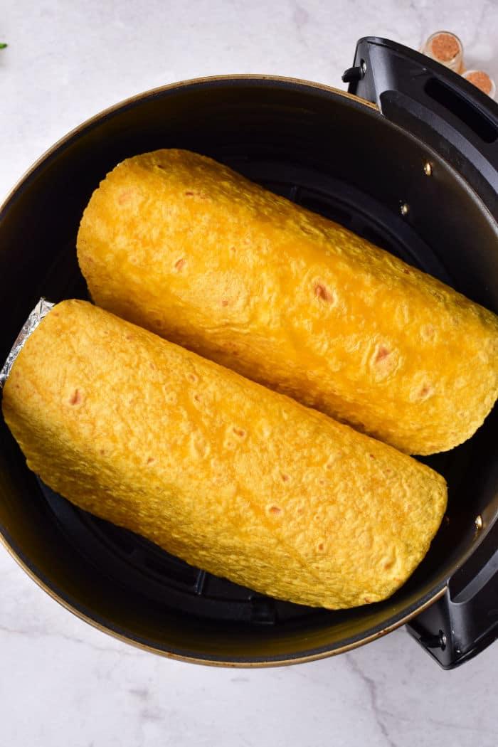 Two yellow tortilla shells wrapped around delicious fillings, nestled side by side in a black cooking pot, reminiscent of taco shells prepared perfectly in an air fryer.