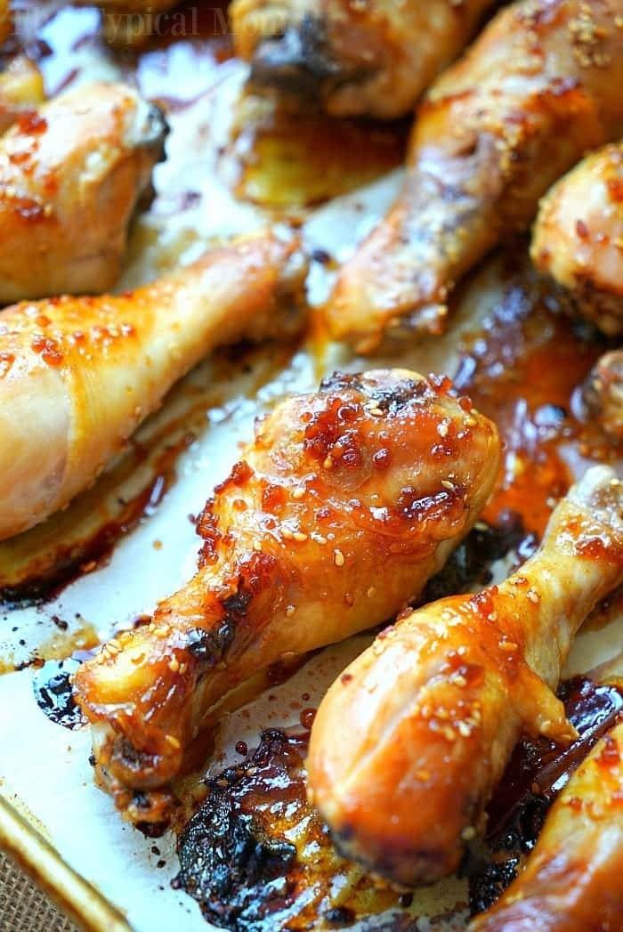 Close-up of teriyaki chicken drumsticks glazed with a sticky sauce, arranged on a baking tray. The drumsticks boast a golden-brown, crispy exterior with visible sesame seeds and caramelized edges.