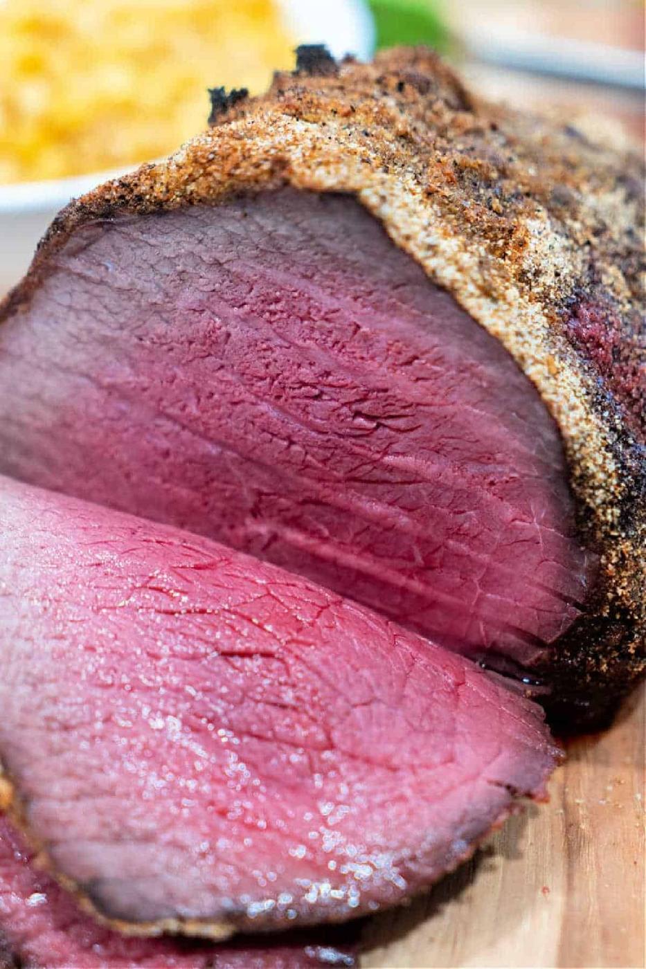 Sliced roast beef with a seasoned crust, cooked rare, showing a juicy pink center on a cutting board—a classic Top Round Roast Recipe done to perfection.
