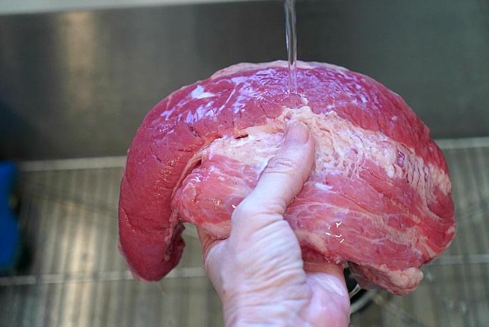 Carefully rinsing a large slab of point cut corned beef under running water in the kitchen sink, prepping it for a delicious meal.