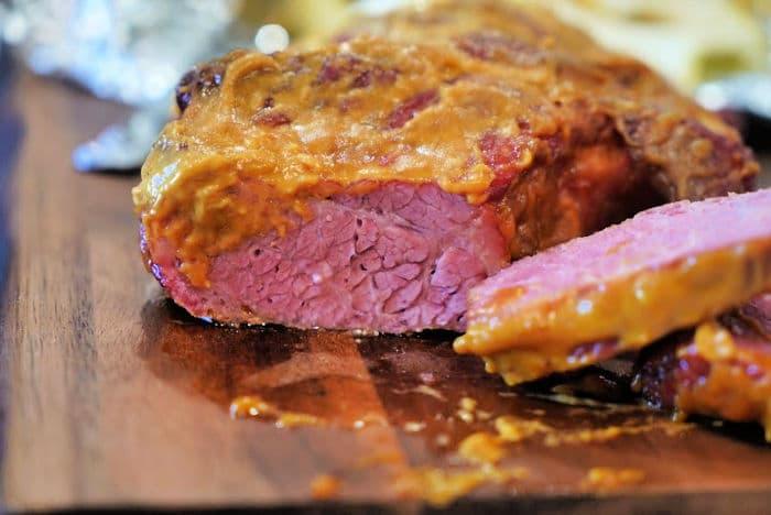 Sliced Traeger corned beef with a mustard crust rests elegantly on a wooden board.