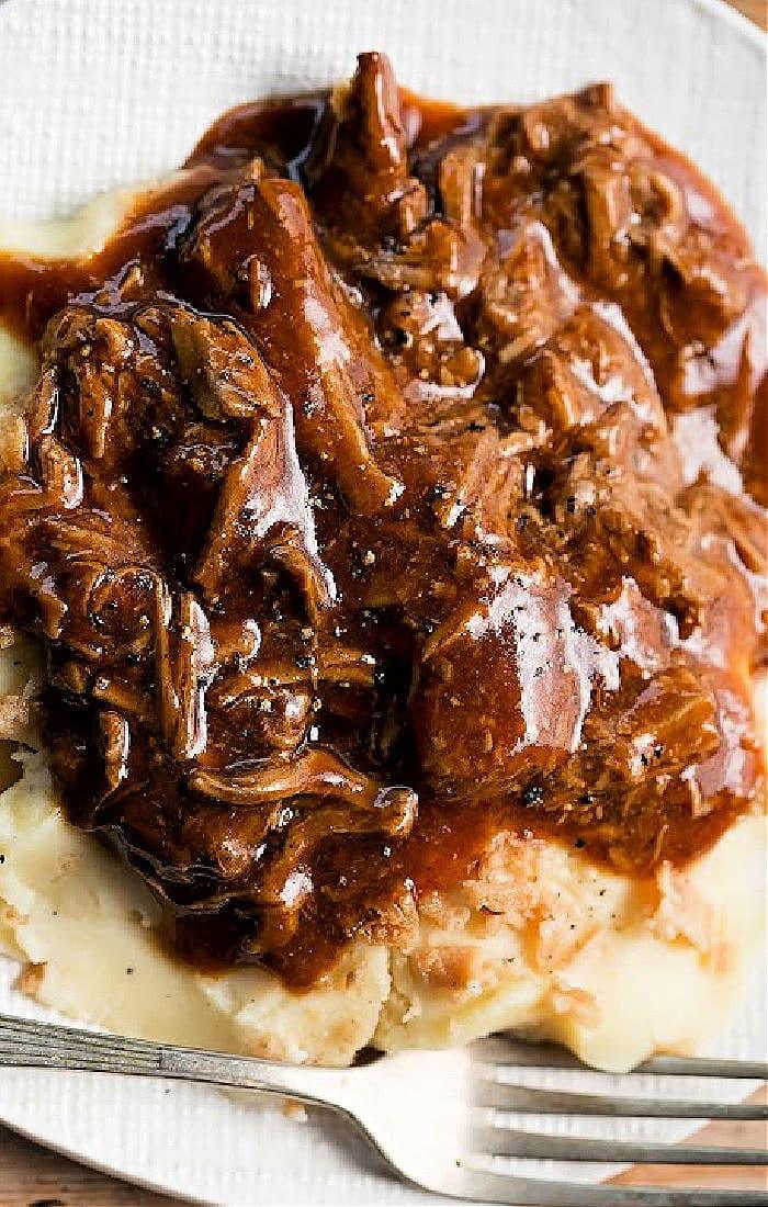Tender rich turkey neck gravy over mashed potatoes on a white plate, accompanied by a fork.