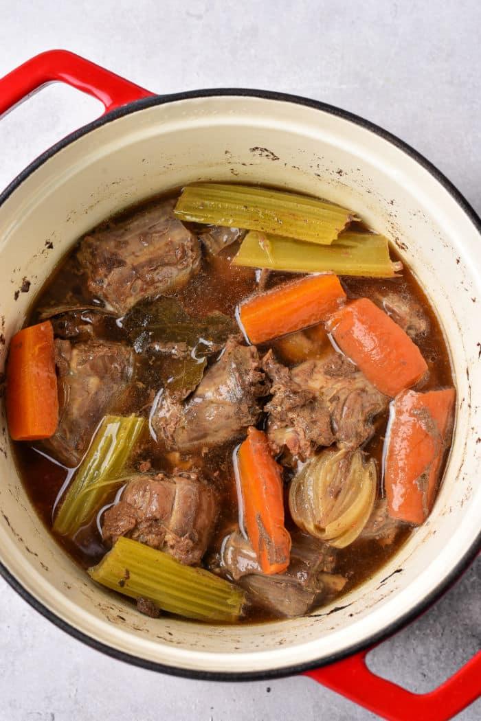 A pot of braised turkey necks, carrots, celery, onion, and broth simmering gently with a hint of turkey neck gravy for added richness.