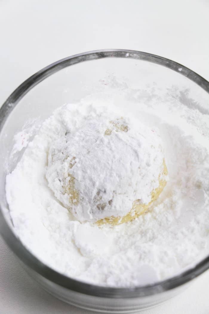 A glass bowl with 3 Ingredient Cake Mix Cookies dough covered in powdered sugar sits on a white surface.